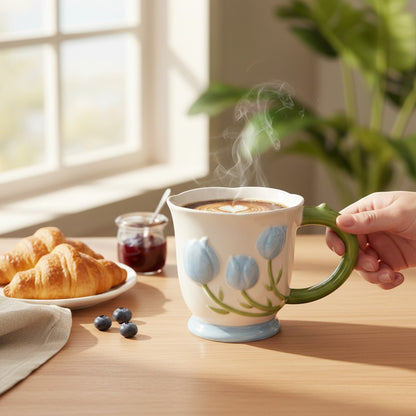 Ayethic blue tulip buds ceramic mug with green handle and scalloped rim. Features raised floral artwork and a cream glaze.