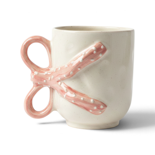 Ayethic handcrafted ceramic mug in cream with a unique pink bow-shaped handle and delicate white polka dot details.