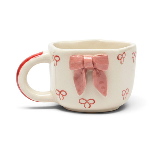 Ayethic handcrafted ceramic mug in cream with a 3D pink bow and small red bow patterns, featuring a red handle.